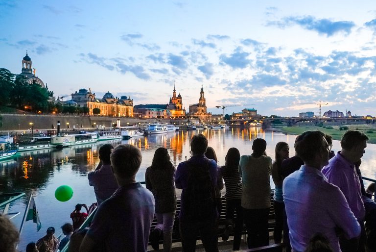Menschen stehen auf der Wissenschaftsfahrt und betrachten die abendliche Elbe / Englisch:People stand on the science cruise and look at the evening Elbe river Logo