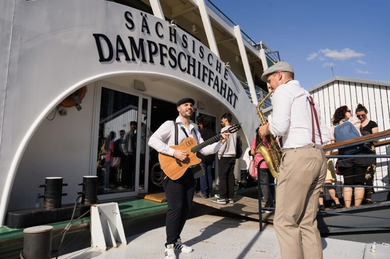 Musiker vor einem Boot mit der Aufschrift Sächsische Dampfschifffahrt.