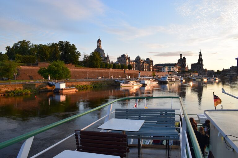 Im Vordergrund eine Bank auf einem Schiff. Im Hintergrund die Stadtkulisse von Dresden.