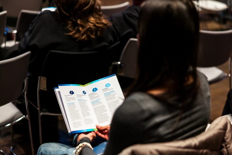 Eine Person hält ein Programmheft in der Hand. Logo