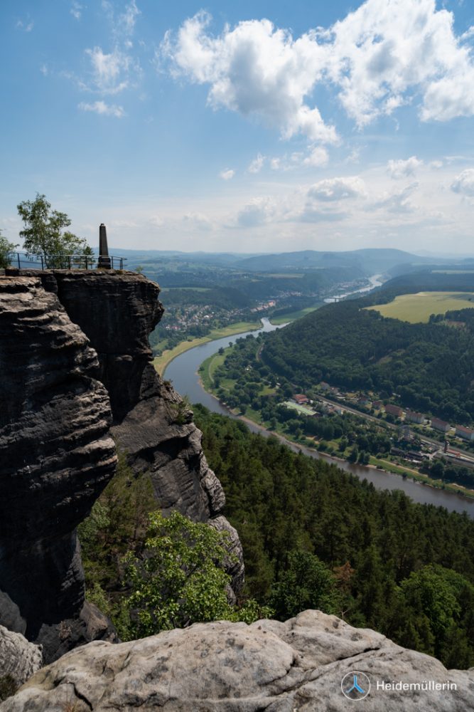View from a rocky mountain onto a monument, with a river flowing in the valley Logo