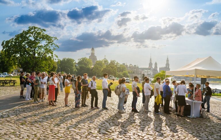 Vor der Stadtkulisse von Dresden seht eine große Menge für eine Registrierung an. Logo