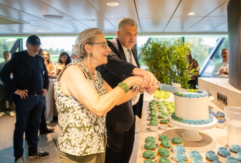 2 Personen schneiden zusammen eine Torte an, die Torte ist umringt von Cupcakes mit grünen und blauen Verzierungen Logo
