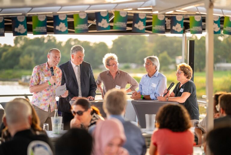 5 Personen stehen an Stehtischen, 2 von ihnen halten Mikrofone in den Händen, eine Person darüber hinaus noch Moderationskarten auf denen das Logo von DRESDEN-concept abgebildet ist. Logo