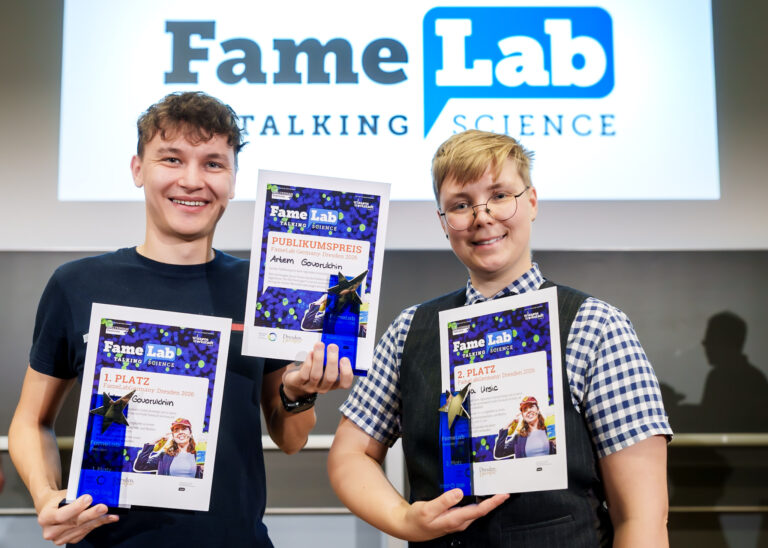 Das Foto zeigt die Gewinner des FameLab Regionalentscheids Dresden 2026: Artem Govorukhin mit Ukrunden und Pokalen für den 1. Platz sowie den Publikumspreis und Urša Uršič für den 2. Platz. Logo