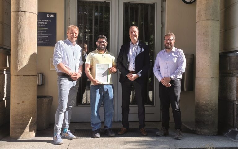 Gruppenfoto von vier Menschen, davon hält eine Person eine Urkunde Logo